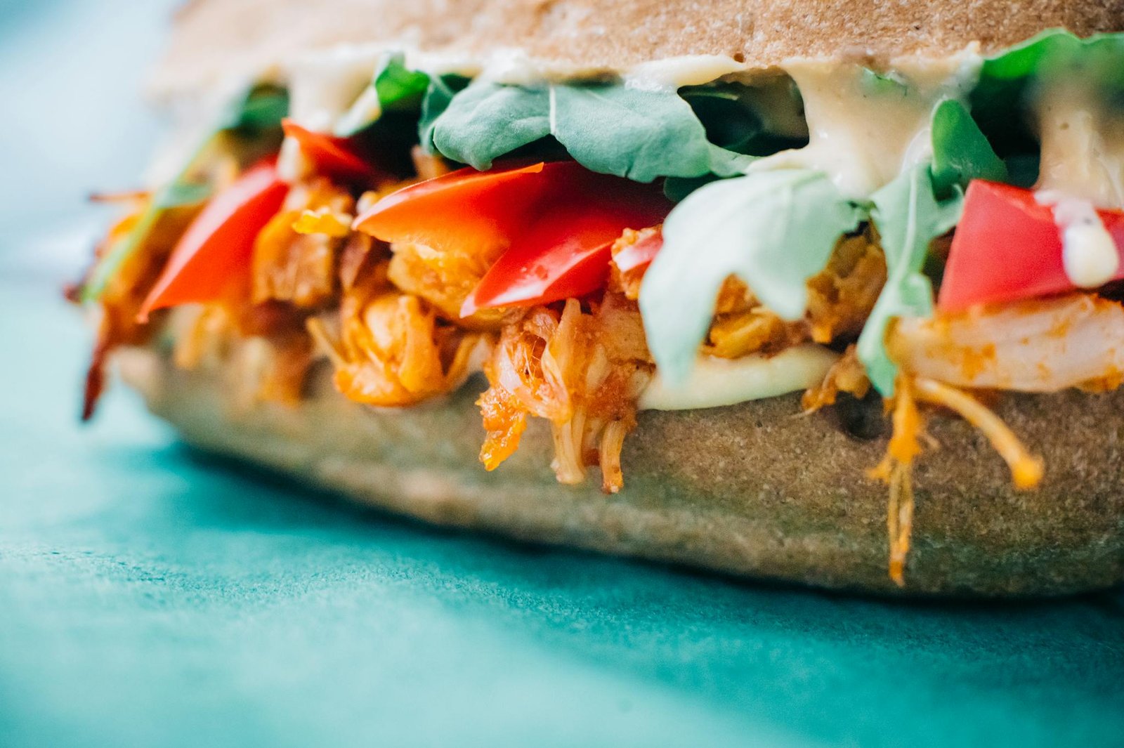 Mouthwatering chicken sandwich with fresh veggies and sauce on colorful background.